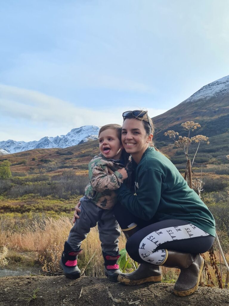 A mom and toddler hugging and smiling while hiking together in a mountainous area